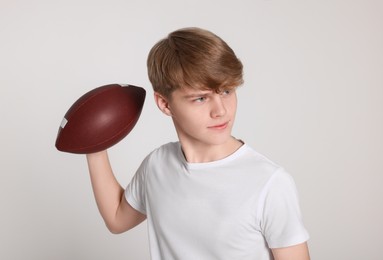 Teenage boy with american football ball on light grey background