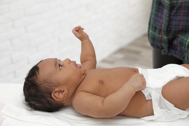 Photo of Cute African-American baby lying on scales indoors