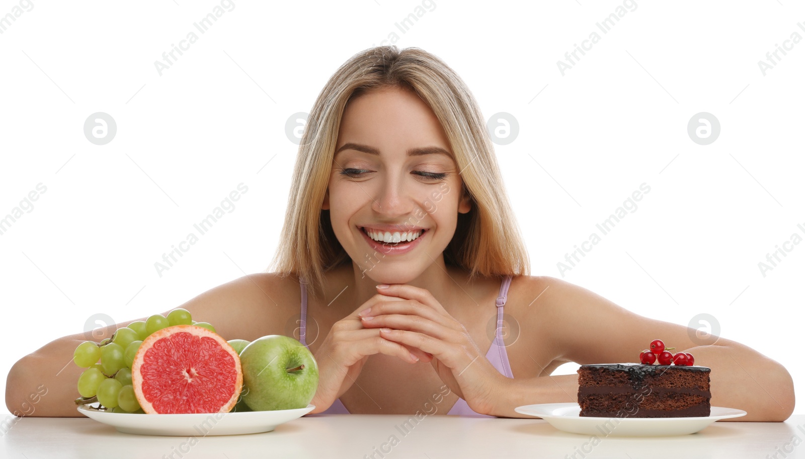 Photo of Woman choosing between cake and healthy fruits at table on white background