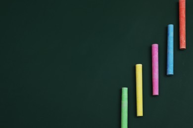 Photo of Colorful chalks on green board, flat lay. Space for text