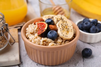 Photo of Bowl of oatmeal with blueberries, almonds, banana and fig pieces on white table, closeup