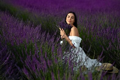 Photo of Beautiful young woman with bouquet sitting in lavender field