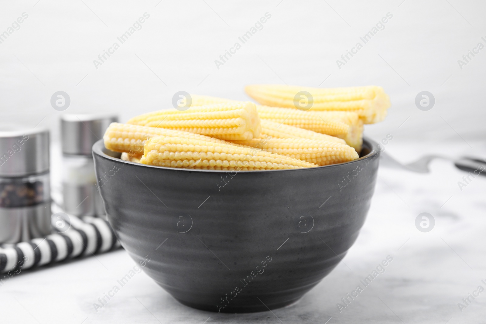 Photo of Bowl of pickled baby corn on white marble table, closeup