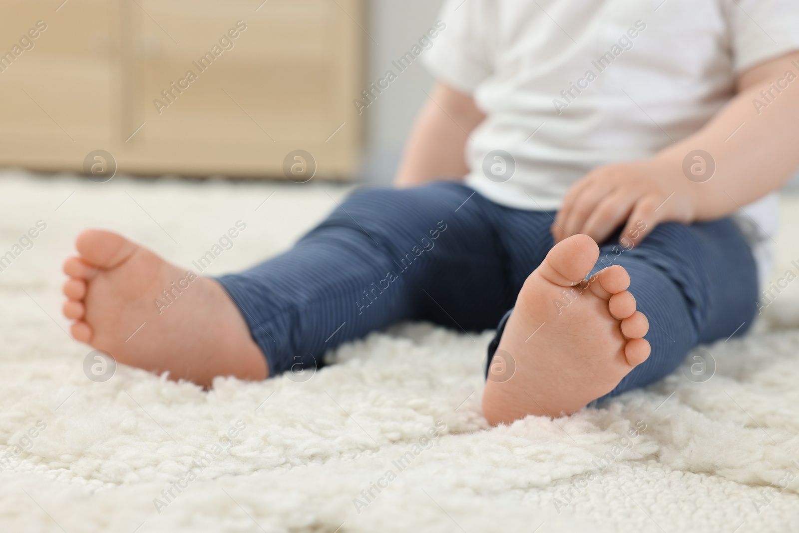 Photo of Baby sitting on soft carpet indoors, closeup