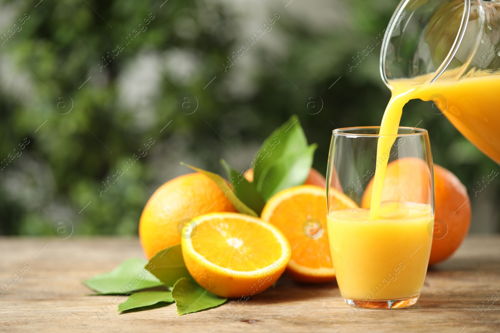 Photo of Pouring orange juice into glass at wooden table. Space for text