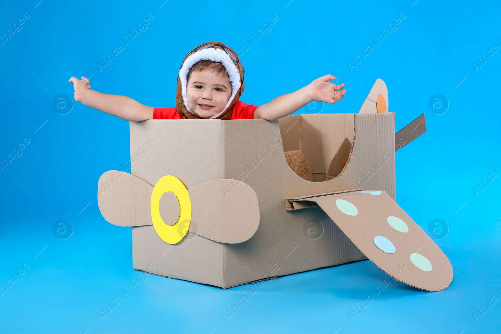 Photo of Cute little child playing with cardboard airplane on light blue background