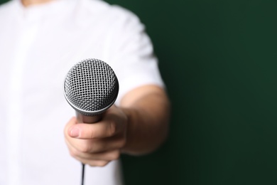 Photo of Young man in casual clothes holding microphone on color background, closeup with space for text