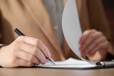 Woman signing documents at table in office, closeup