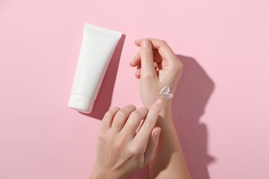 Photo of Woman with tube applying cosmetic cream onto her hand on pink background, top view