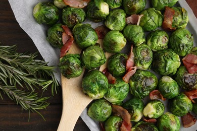 Photo of Delicious roasted Brussels sprouts, bacon, rosemary and spatula on wooden table, top view