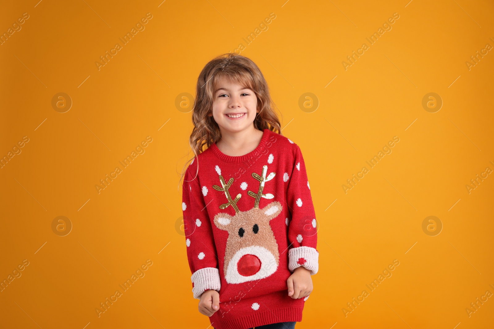 Photo of Cute little girl in red Christmas sweater smiling against orange background