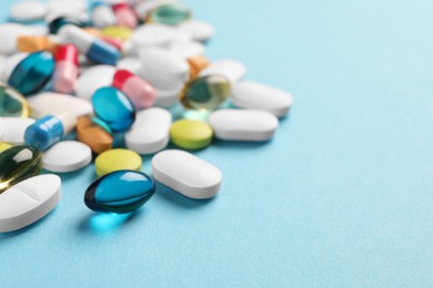 Pile of different pills on light blue background, selective focus. Space for text