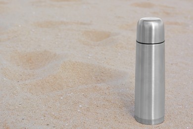 Photo of Metallic thermos with hot drink on sandy beach, space for text