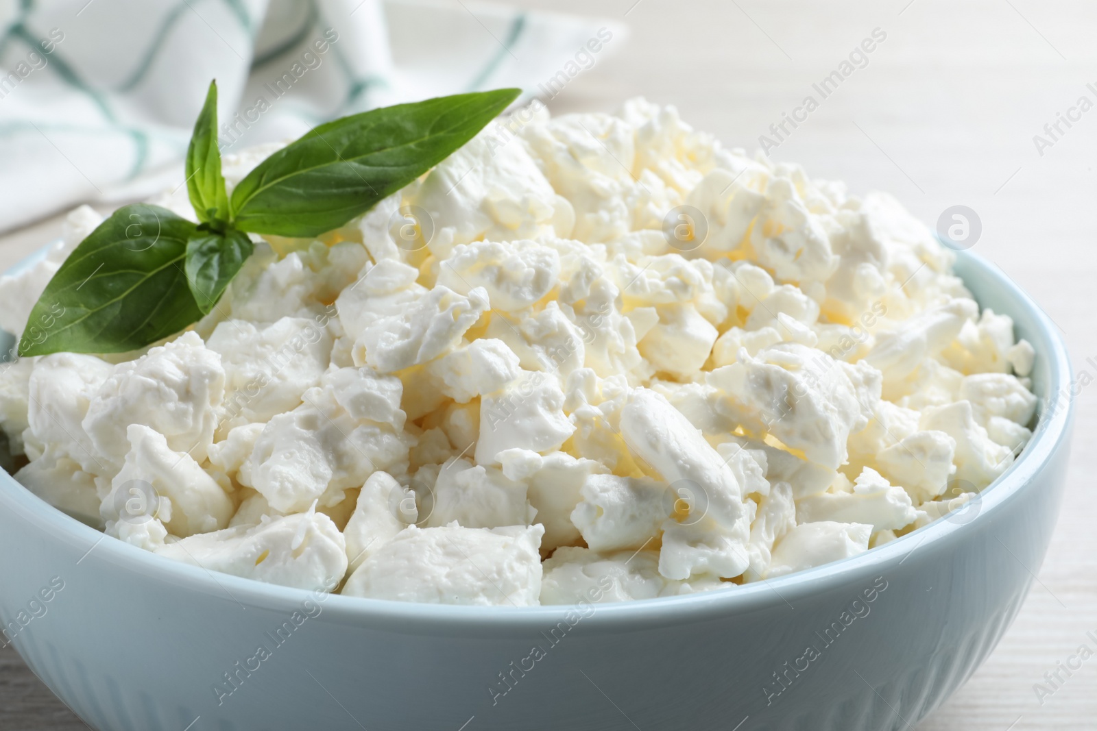 Photo of Fresh cottage cheese with basil in bowl, closeup