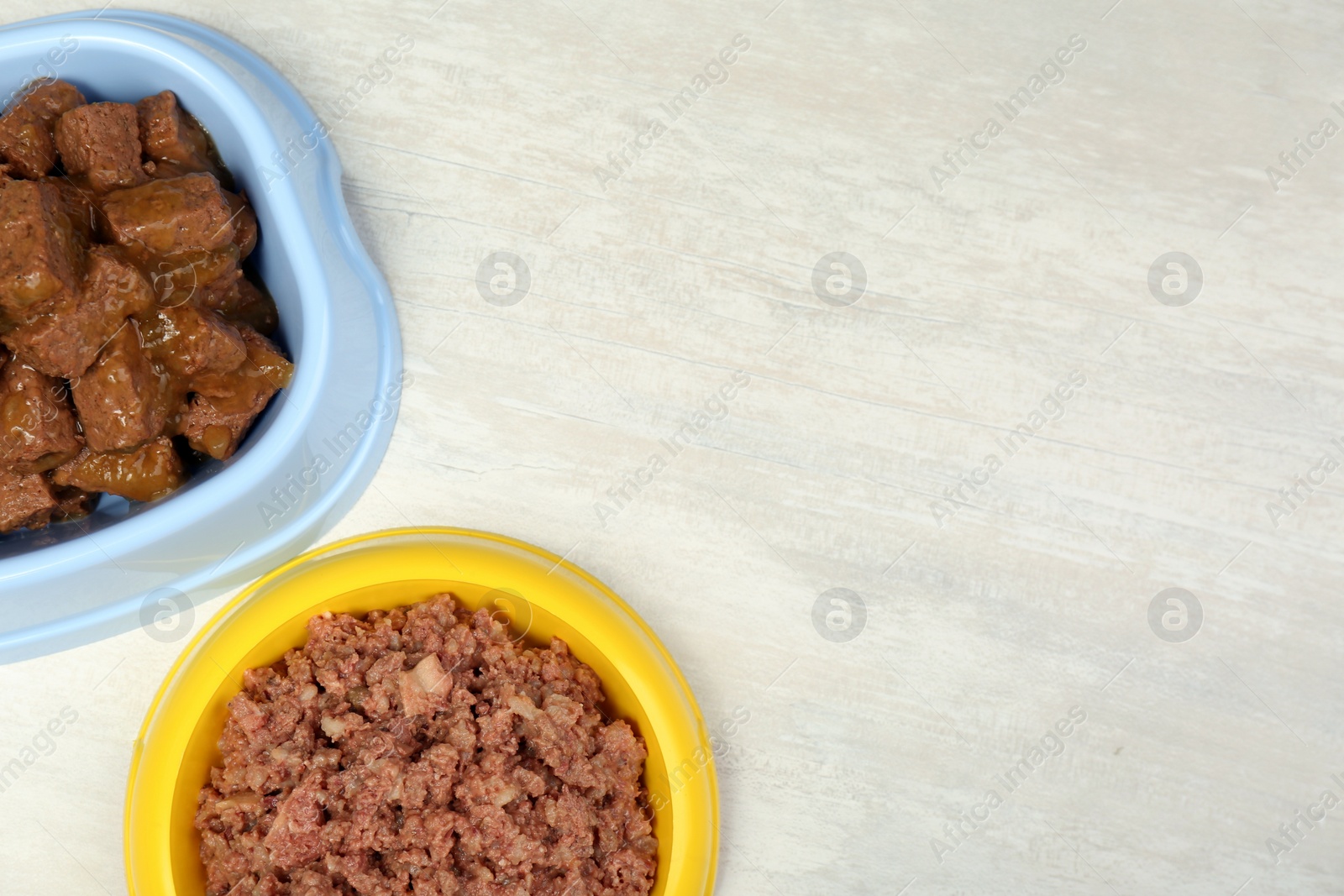 Photo of Different pet food in feeding bowls on white table, flat lay. Space for text