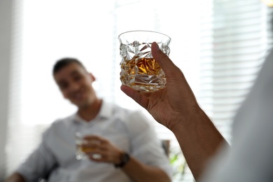 Photo of Young men drinking whiskey together at home