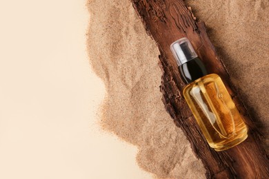 Photo of Bottle of serum and tree bark on sand against beige background, top view. Space for text