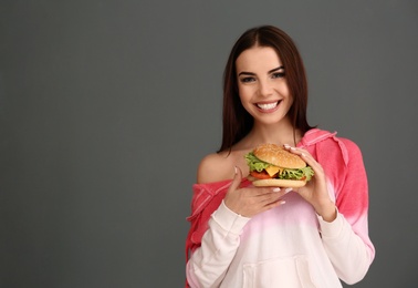 Photo of Young woman with tasty burger on grey background. Space for text