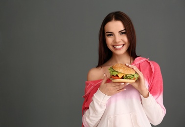 Young woman with tasty burger on grey background. Space for text