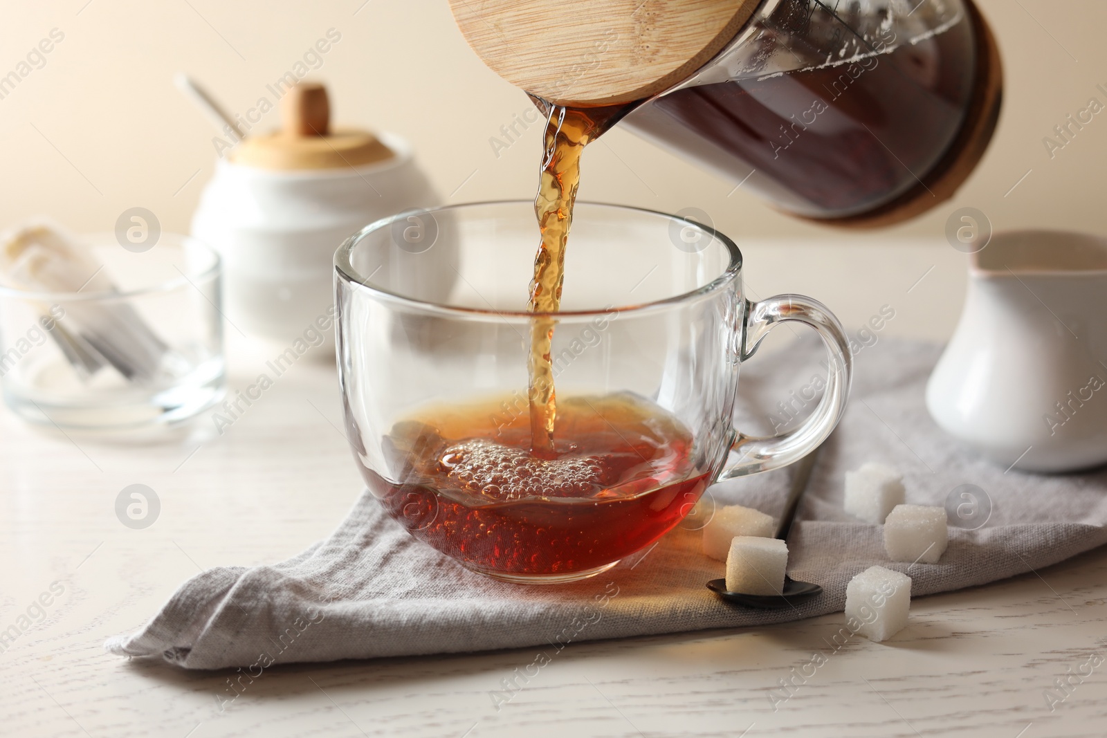 Photo of Pouring warm tea into cup on white wooden table, closeup