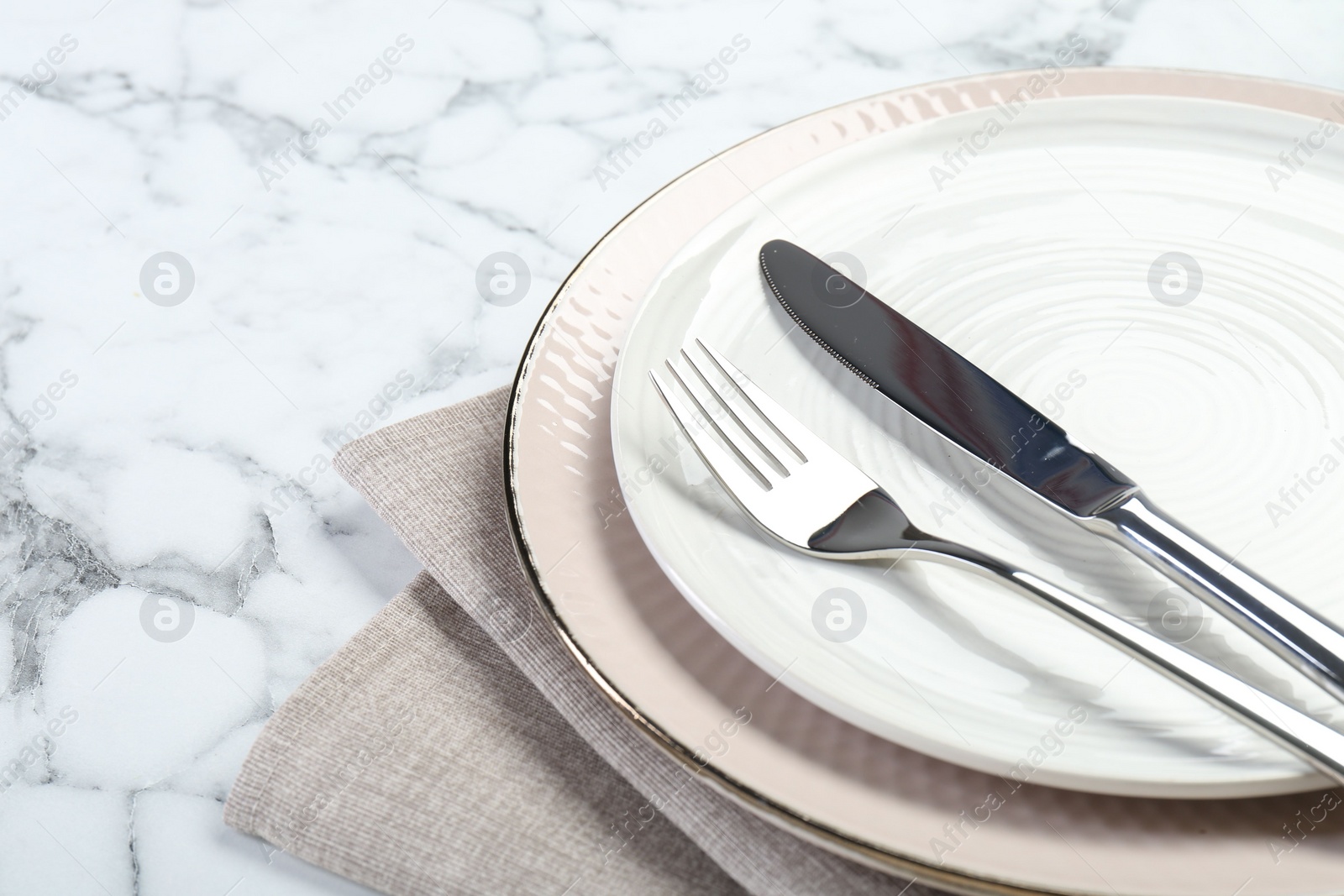 Photo of Clean plates, cutlery and napkin on white marble table, closeup. Space for text