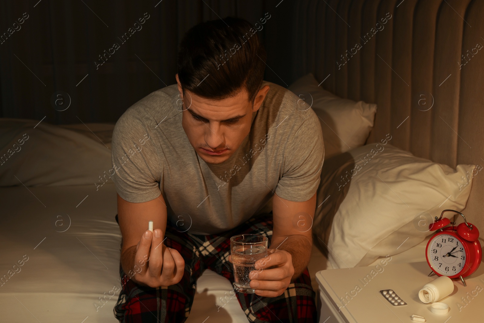 Photo of Man suffering from insomnia taking pill on bed at night