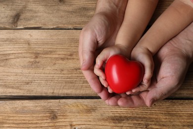 Father and his child holding red decorative heart at wooden table, top view. Space for text