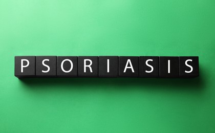 Photo of Word Psoriasis made of black wooden cubes with letters on green background, top view