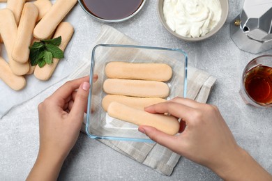 Woman making tiramisu cake at light grey table, top view