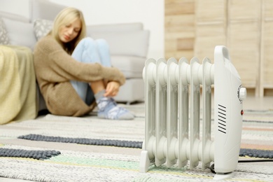 Photo of Electric heater and blurred young woman on background. Space for text