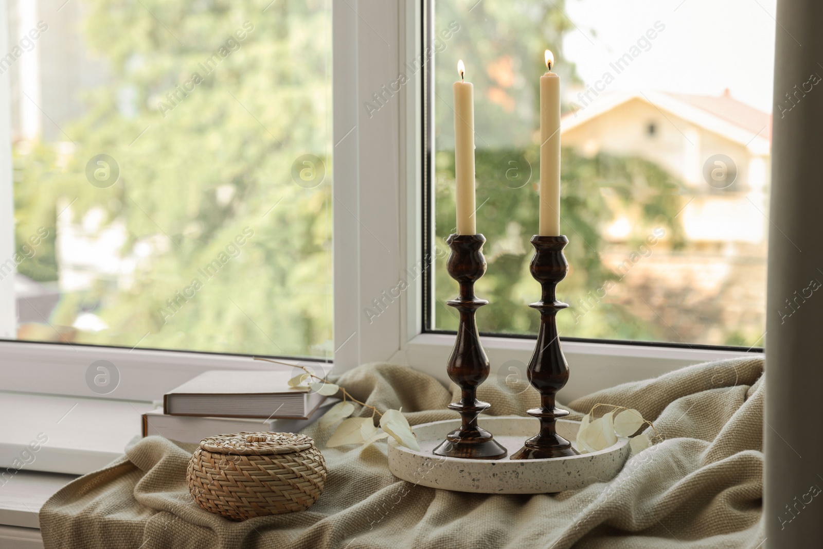 Photo of Pair of beautiful black candlesticks, books and round wicker box on windowsill