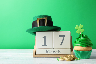 Decorated cupcake, wooden block calendar, hat and coins on white table. St. Patrick's Day celebration