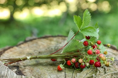 Photo of Bunch with tasty wild strawberries on wooden stump outdoors