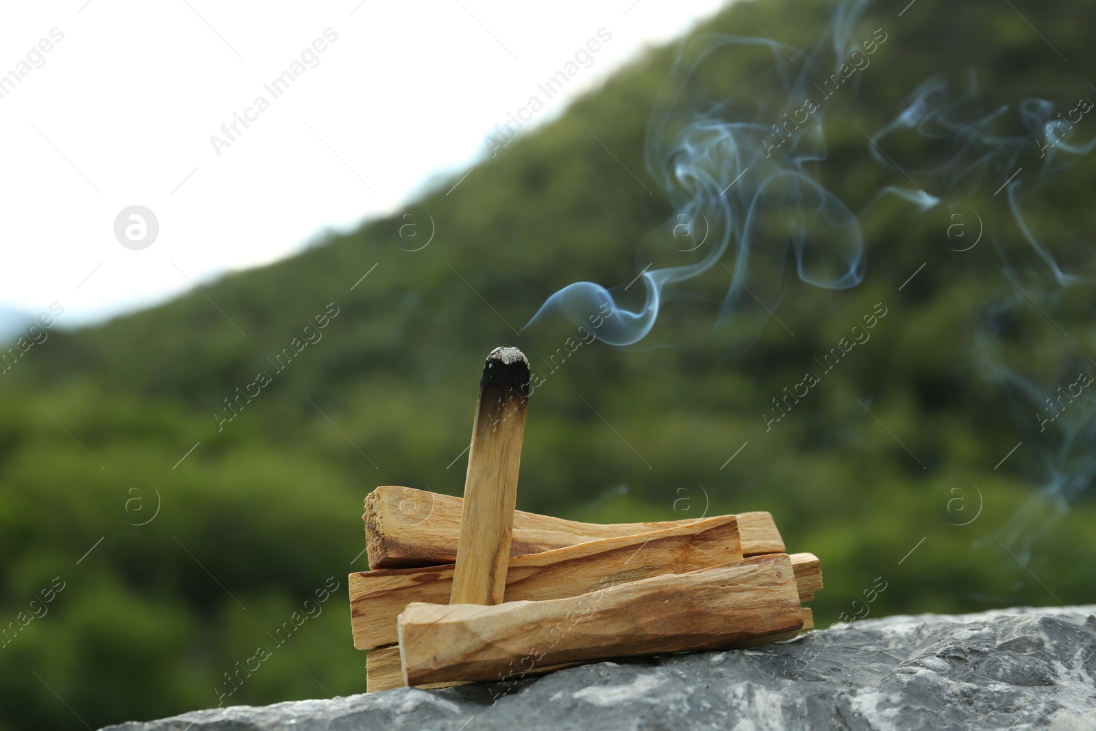 Photo of Burning palo santo stick on stone surface outdoors, closeup