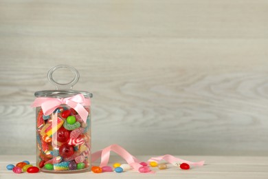 Photo of Jar with different delicious candies on beige wooden table, space for text
