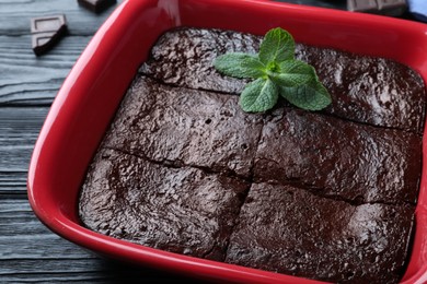 Photo of Delicious chocolate brownie with mint in baking dish on black wooden table, closeup