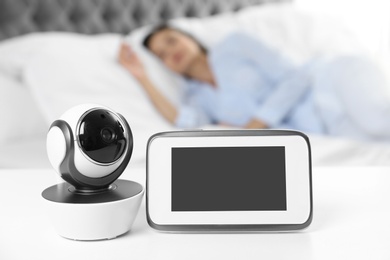Photo of Baby monitor and camera on table near bed with woman in room. Video nanny