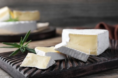 Photo of Tasty cut brie cheese with rosemary on wooden board, closeup