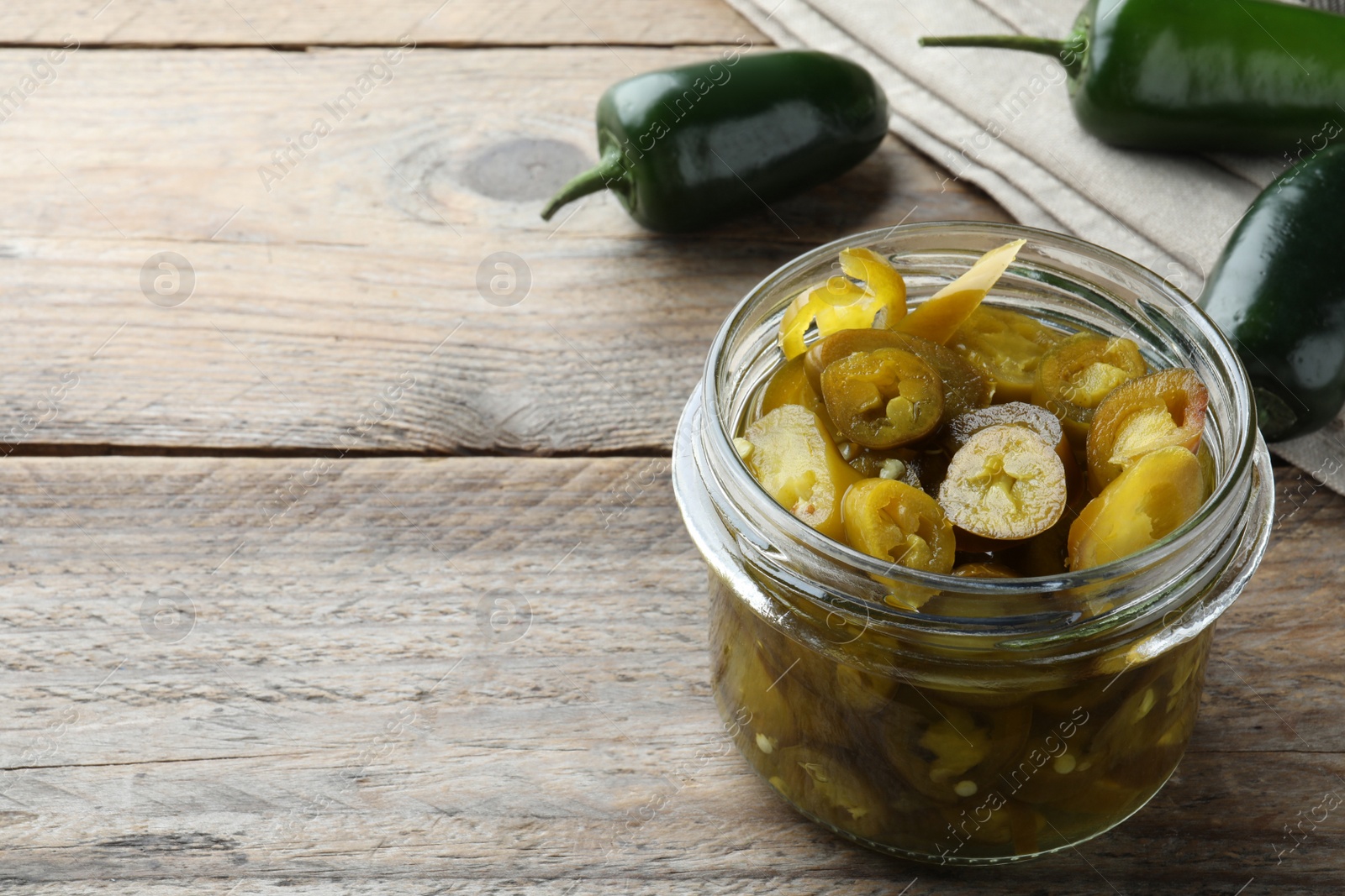 Photo of Fresh and pickled green jalapeno peppers on wooden table, space for text