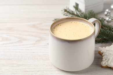 Cup of delicious eggnog on wooden table, space for text