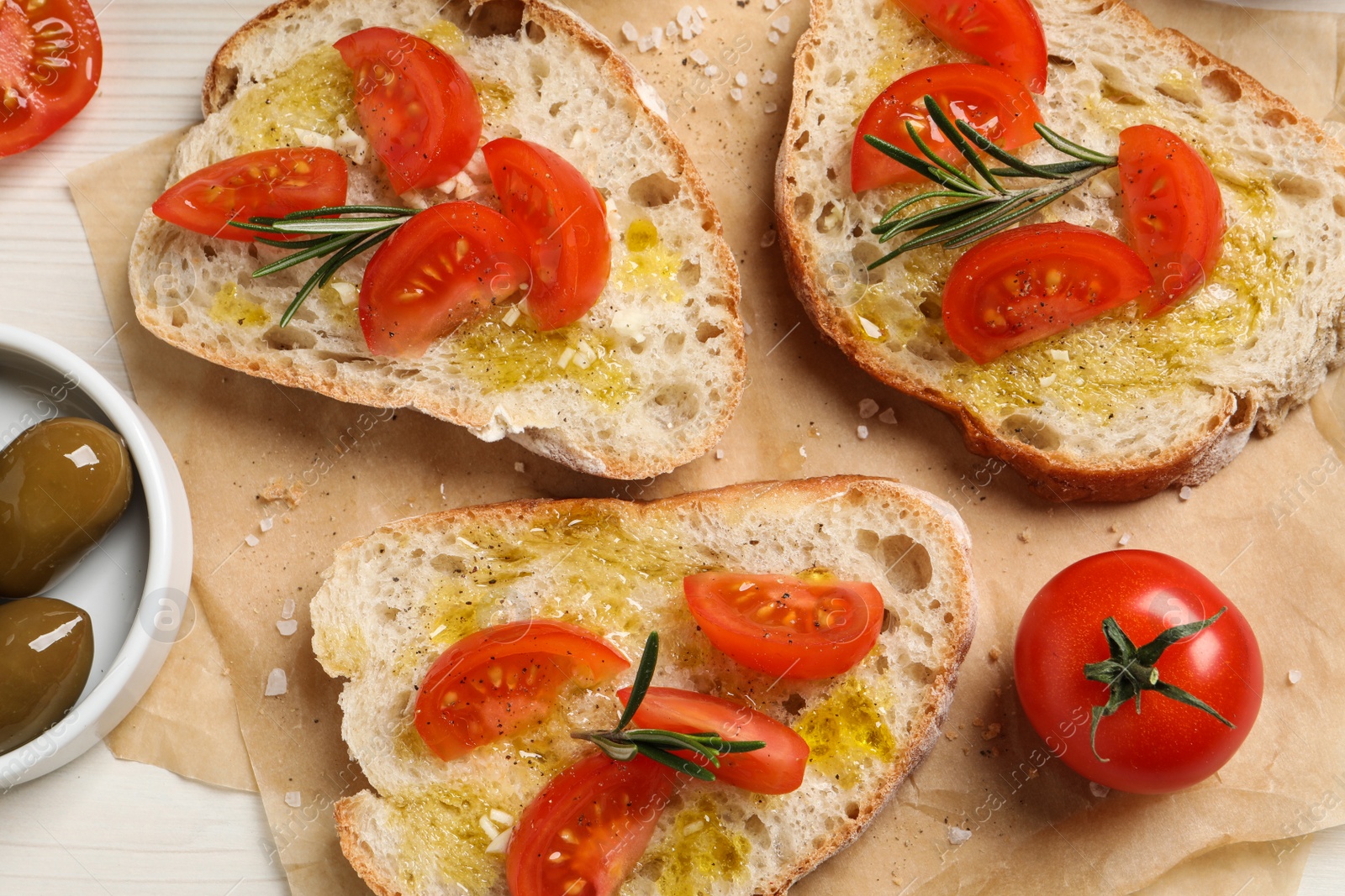 Photo of Tasty bruschettas with oil, tomatoes and rosemary on parchment paper, flat lay