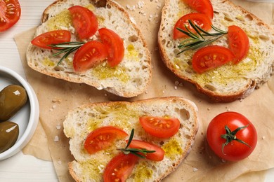 Photo of Tasty bruschettas with oil, tomatoes and rosemary on parchment paper, flat lay