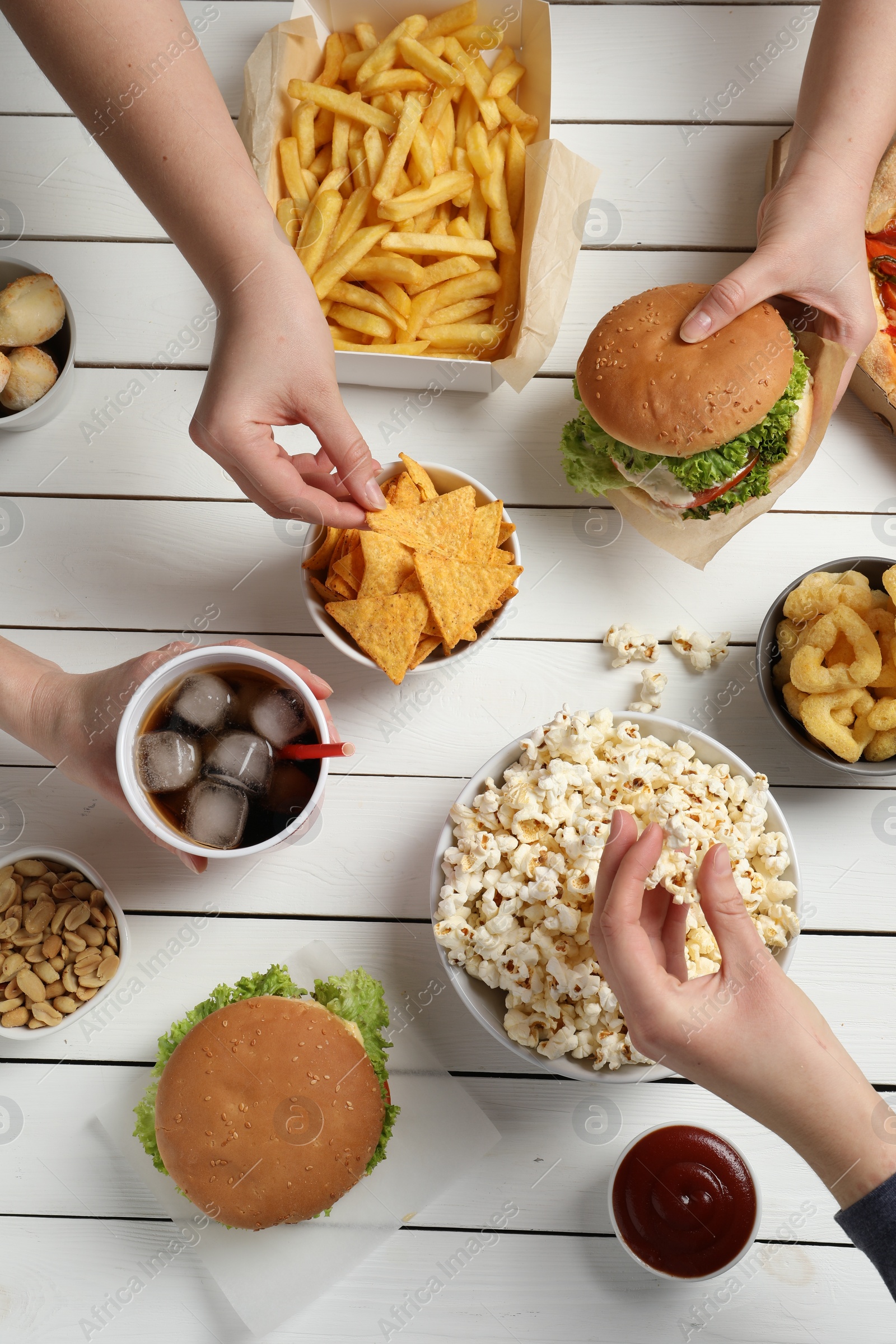 Photo of Friends eating burger, popcorn and other fast food at white wooden table, top view