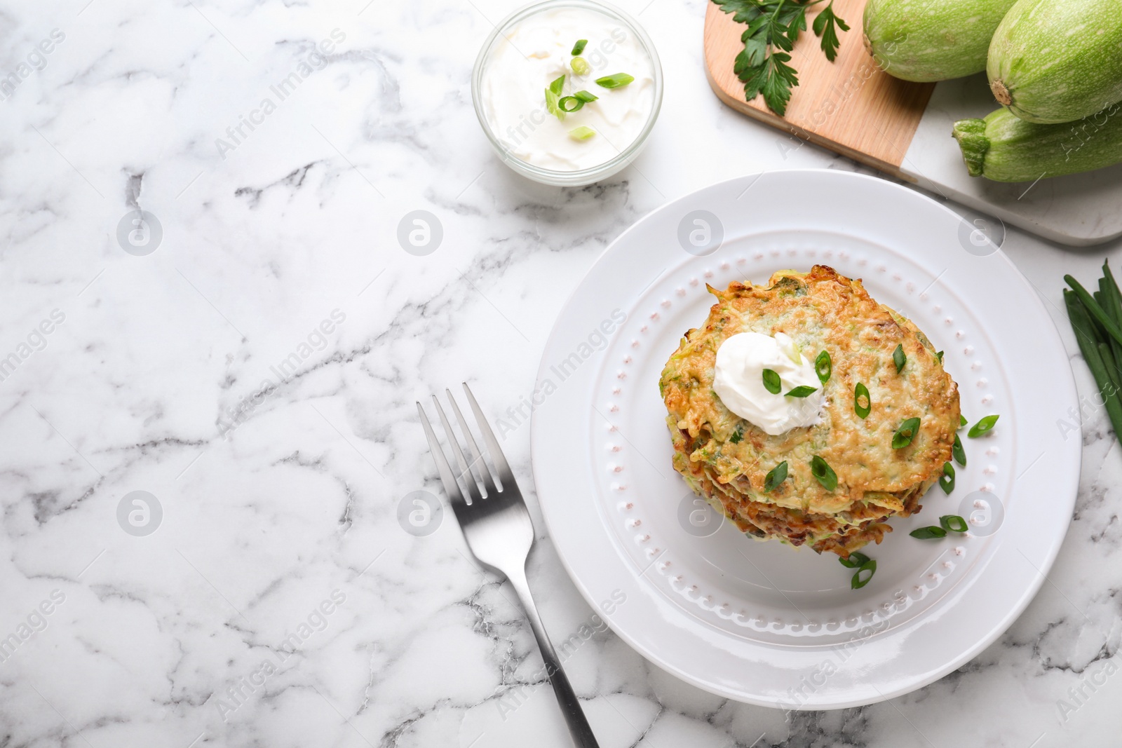 Photo of Delicious zucchini fritters served on white marble table, flat lay. Space for text
