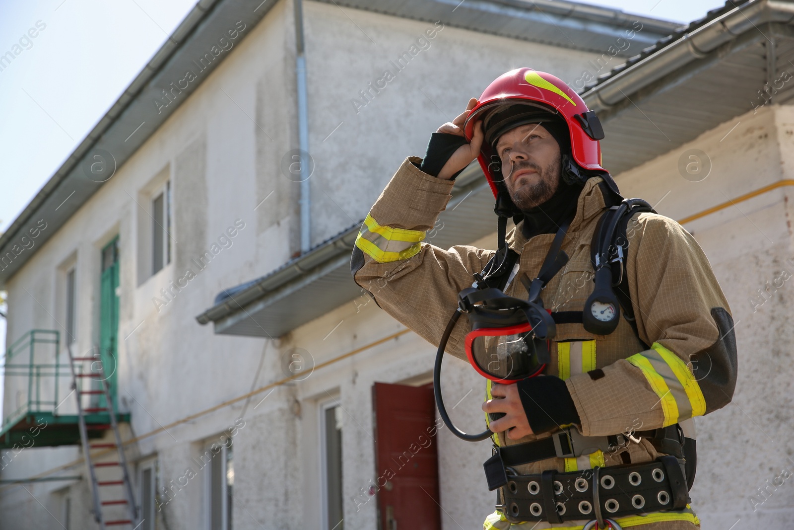 Photo of Firefighter in uniform with helmet near station outdoors, space for text