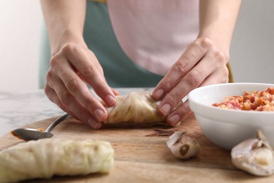 Woman preparing stuffed cabbage roll at table, closeup