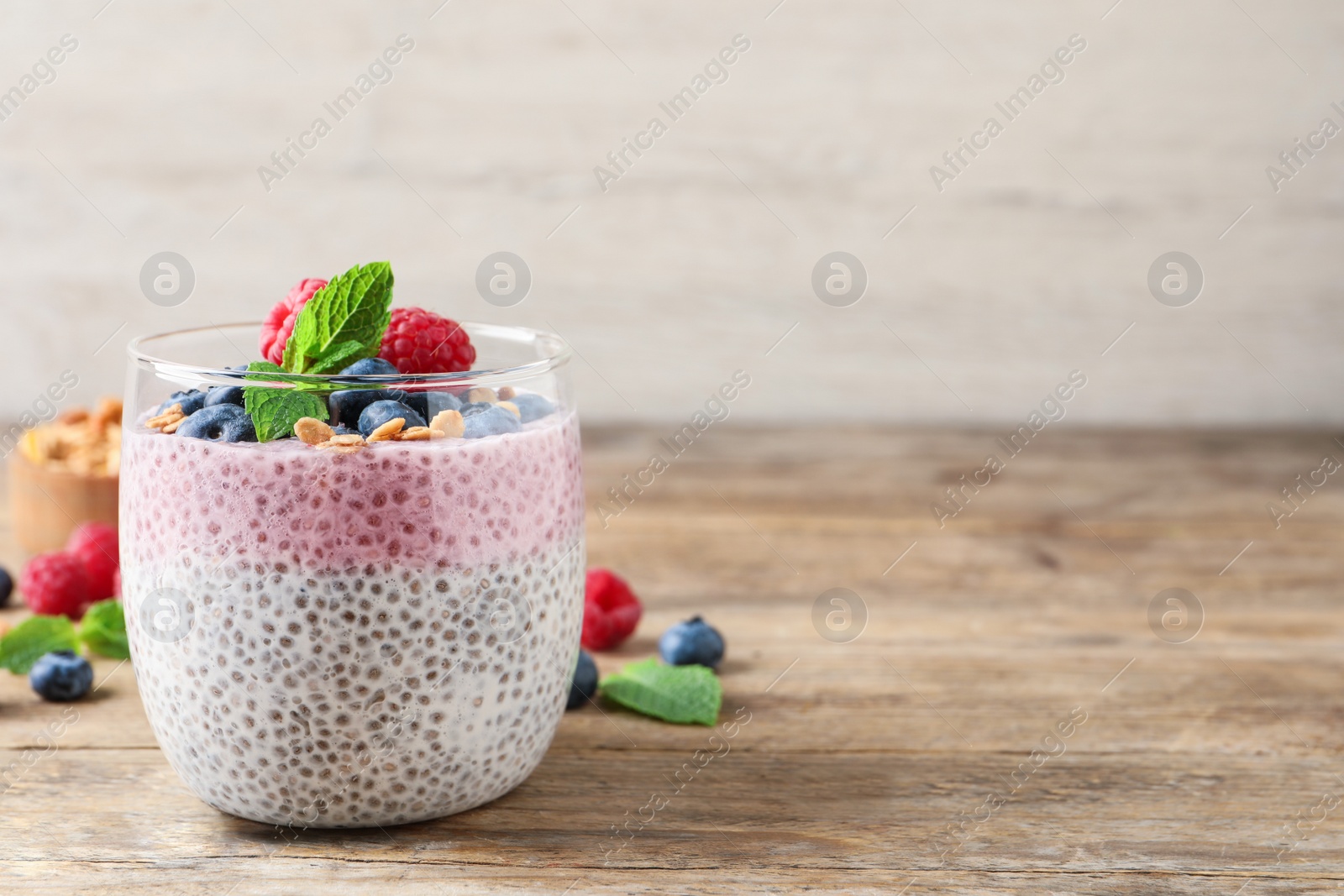 Photo of Delicious chia pudding with berries, granola and mint on wooden table, space for text