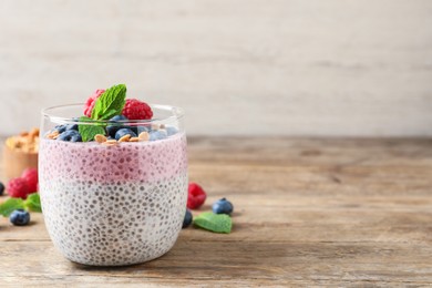 Photo of Delicious chia pudding with berries, granola and mint on wooden table, space for text