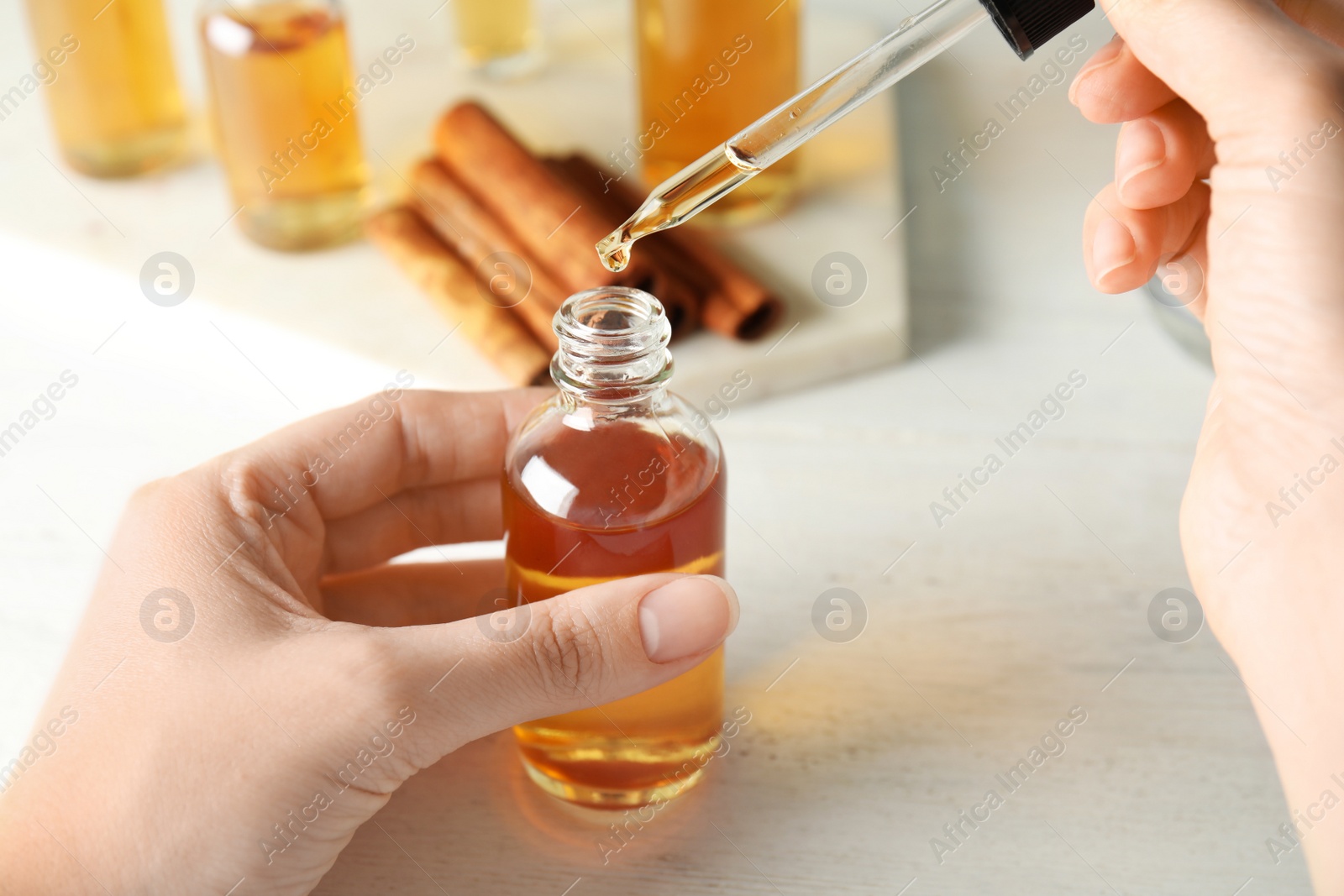 Photo of Woman dripping cinnamon essential oil from pipette into bottle at table, closeup