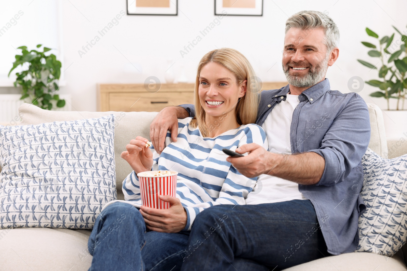 Photo of Happy affectionate couple with popcorn on sofa at home, space for text. Romantic date